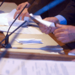 men holding papers in front of microphone